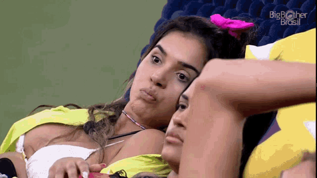 two women laying on a couch with big brother brasil on the screen