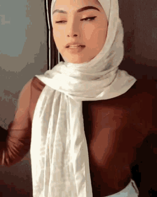 a woman wearing a white hijab and a brown shirt is standing in front of a door .