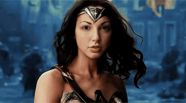 a woman in a wonder woman costume looks at the camera with her hair blowing in the wind