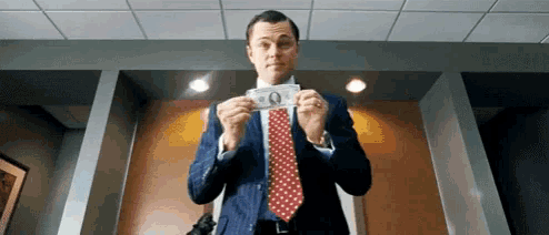 a man in a suit and tie holds a dollar bill