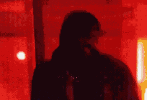 a man in a fur coat is standing in front of a red wall and looking at the camera .