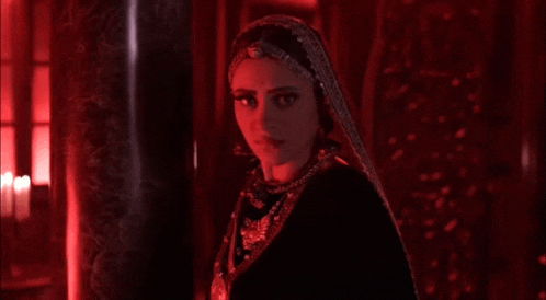 a woman in a black dress and veil is standing in a dark room with red lights behind her .