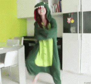 a girl in a green dinosaur costume is dancing in a kitchen