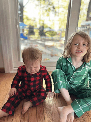 a boy in green pajamas sits next to a crying baby
