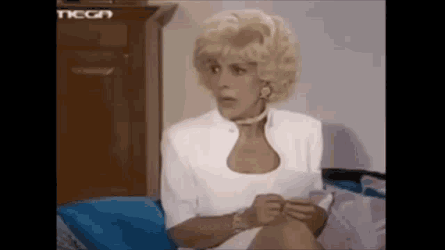 a woman in a white dress is sitting on a couch talking to someone .