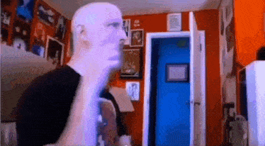a bald man is standing in front of a blue door in a room .