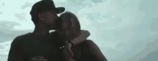 a man and a woman are kissing against a cloudy sky .