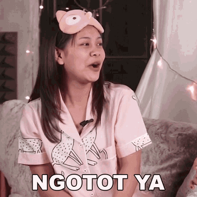 a woman with a sleep mask on her head is sitting on a couch and says ngotot ya