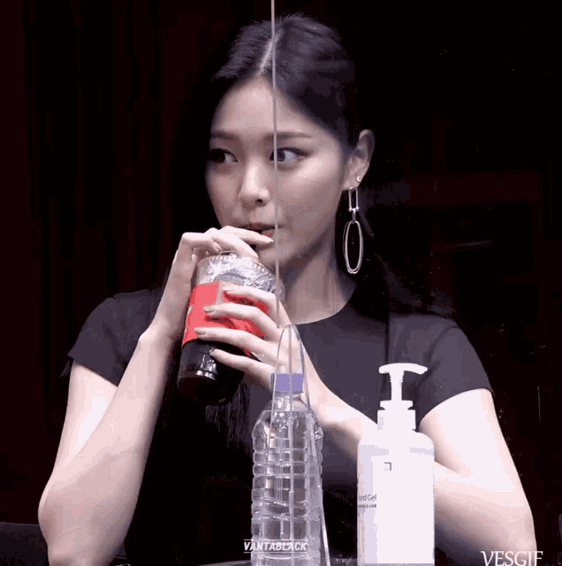 a woman drinking from a plastic cup that says vantablack on it