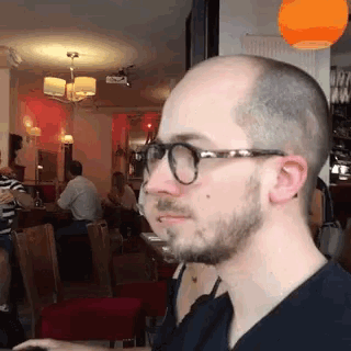 a man with glasses and a beard is sitting at a table in a restaurant
