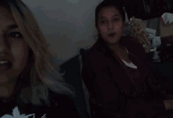 two women are sitting next to each other on a couch and one is wearing a red jacket .