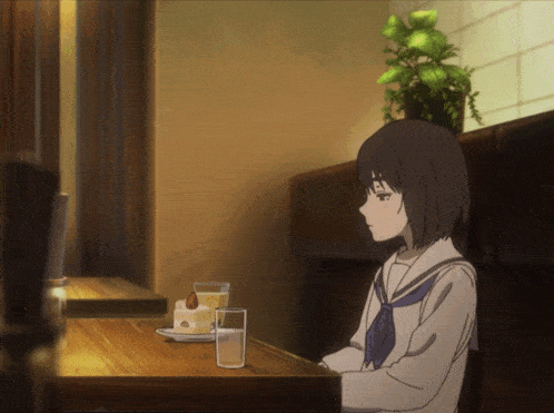 a girl sits at a table with a glass of water and a piece of cake on it