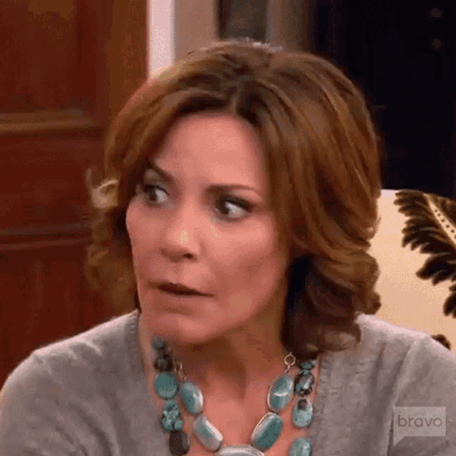 a woman wearing a turquoise necklace and a gray sweater is making a funny face .