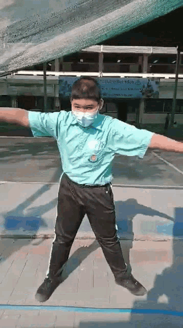 a boy wearing a mask and a blue shirt is standing on a tennis court .