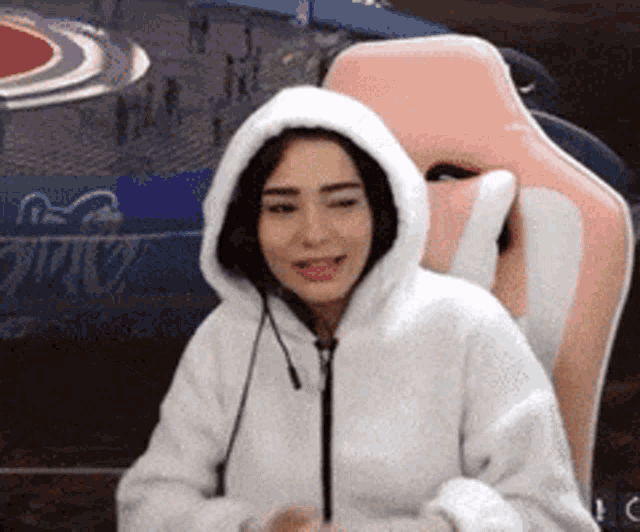 a woman is wearing a white hoodie and sitting in a pink chair .