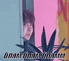 a man is peeking out from behind a door next to a plant and a pink wall .
