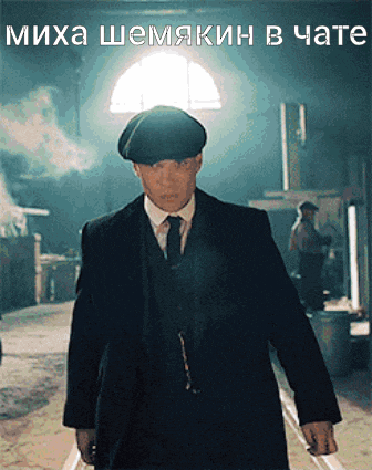 a man in a suit and hat is standing in front of a sign that says " misha shemakin in chate "