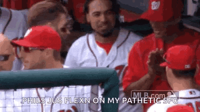 a group of baseball players are sitting in the dugout and one of them is talking to another player .