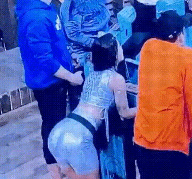 a woman in a blue top and shorts is kneeling down in front of a group of people in a room .