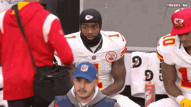 a man wearing a nfl hat sits next to a football player