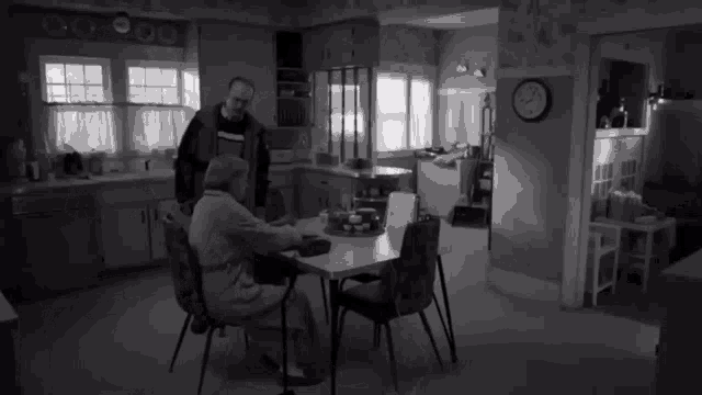 a black and white photo of two people in a kitchen with a clock on the wall