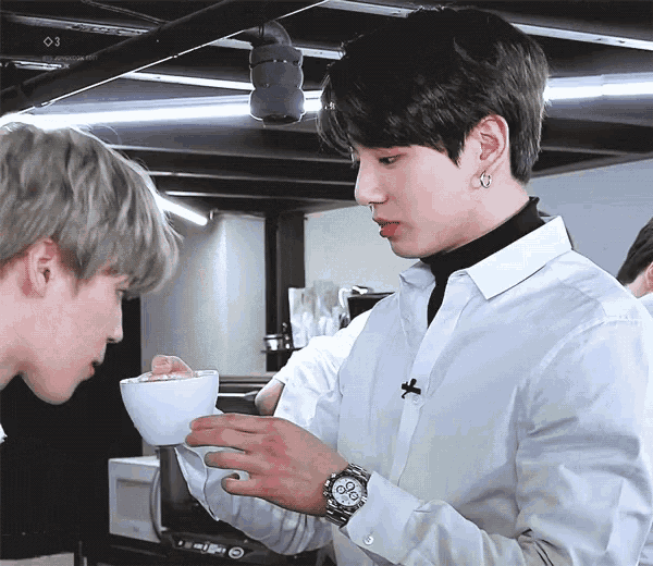 a man in a white shirt is holding a cup of coffee while another man looks on