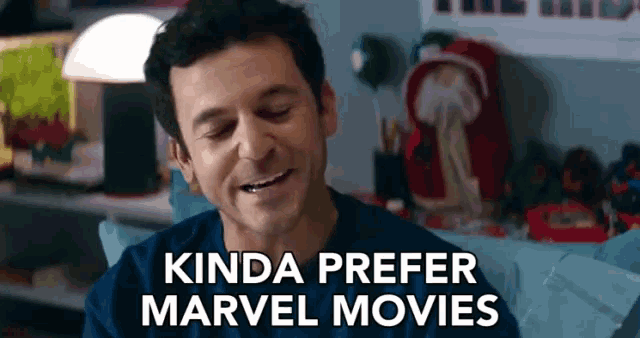 a man is sitting on a couch and smiling with the words `` kinda prefer marvel movies '' above him .