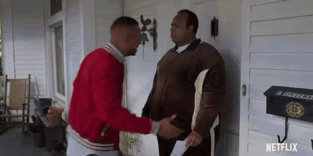 two men are shaking hands on a porch in front of a white house .
