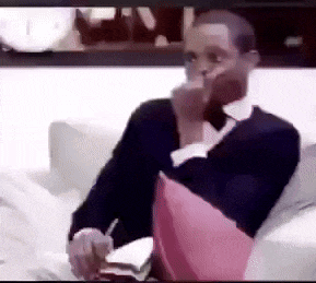 a man is sitting on a couch with a pink pillow and smoking a cigarette .