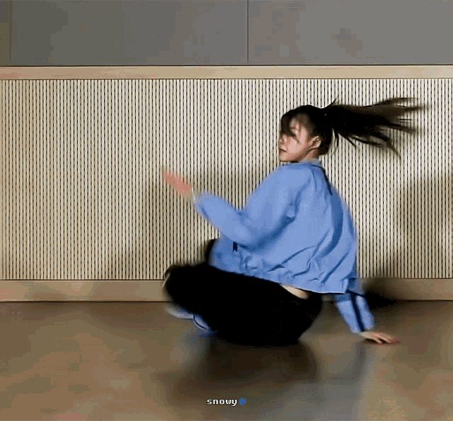 a woman in a blue jacket is kneeling on the floor in front of a wall that says snowy