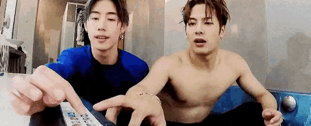 two shirtless men are sitting next to each other in a bathtub .