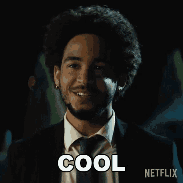 a man in a suit and tie is smiling and the word cool is on the screen behind him