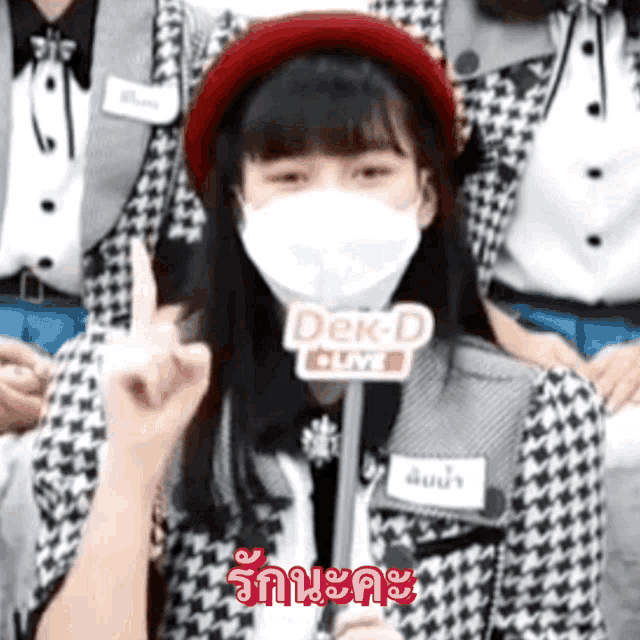 a woman wearing a mask holds up her middle finger in front of a sign that says dek-d live