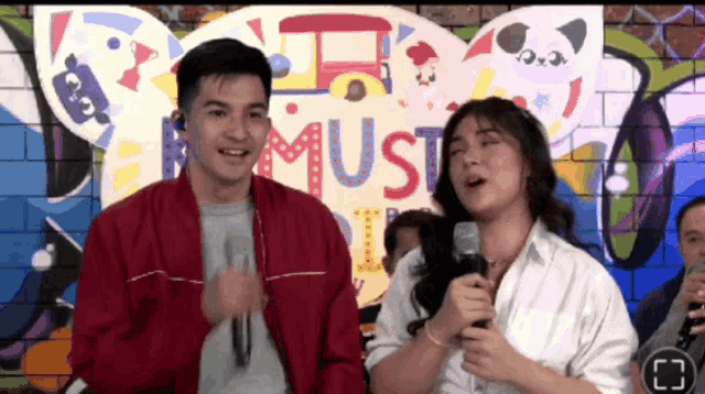 a man and a woman singing in front of a sign that says must