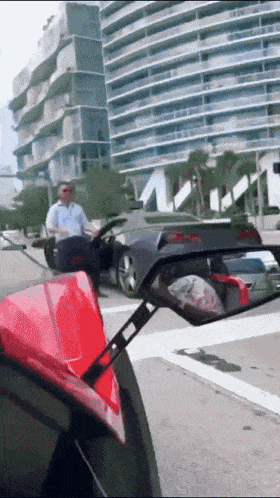 a man sitting in a car looking at another car in a rear view mirror