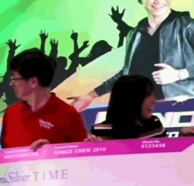 a man in a red shirt stands in front of a dance crew sign
