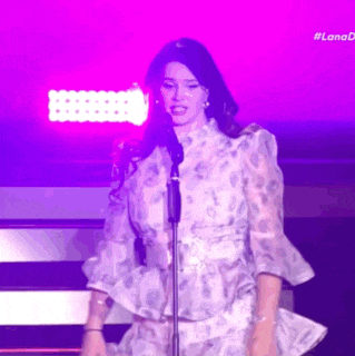 a woman in a white dress is singing into a microphone on a stage with purple lights behind her