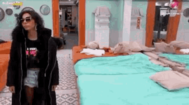 a woman in a black coat and sunglasses is standing in a bedroom with a lot of beds .
