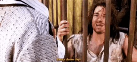 a man with long hair and a beard is behind bars and smiling .