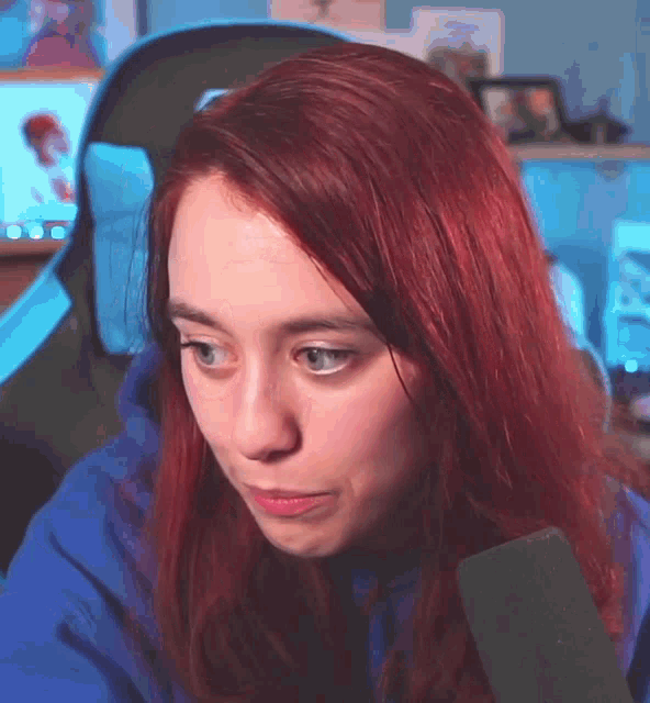a woman with red hair and blue eyes is sitting in a chair with a microphone in front of her .