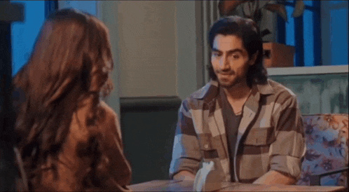 a man and a woman are sitting at a table in a restaurant and talking to each other .