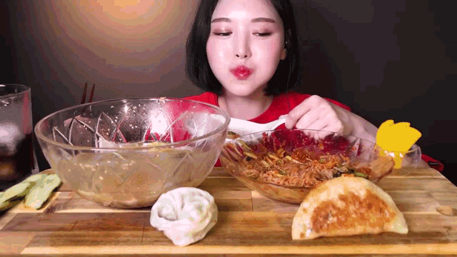 a woman in a red shirt is eating a bowl of food on a wooden table