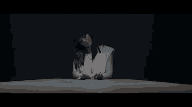 a woman in a white shirt is sitting at a table in a dark room .