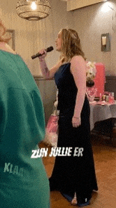 a woman in a black dress is singing into a microphone while standing in a room .