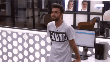 a man wearing a t-shirt that says canjoc is standing in front of a computer monitor