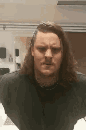 a man with long hair and a beard is wearing a black shirt and making a face .