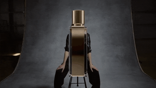 a woman sits on a stool with her legs crossed in front of a large bottle of perfume