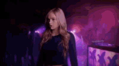 a woman is walking in a dark room with purple lights .