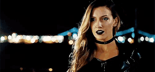 a woman wearing a choker and a leather jacket is standing in front of a bridge .