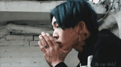 a young man with blue hair is praying with his hands folded in front of his face .